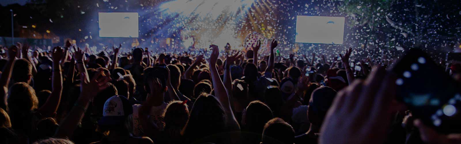 Folla entusiasta a un concerto notturno all’aperto, con luci sul palco, coriandoli nell’aria e molte persone che filmano con i telefoni.